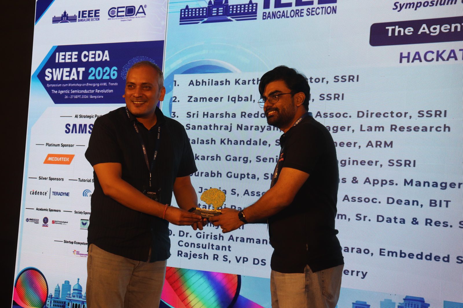 Palash Khandale receiving a memento on stage at IEEE CEDA SWEAT 2026, with the hackathon mentors list on the screen behind him
